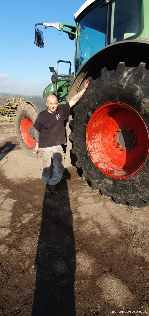 Nortons fitter beside a tractor rear wheel on a farm, close view Nortons fitter beside a tractor rear wheel on a farm, close view