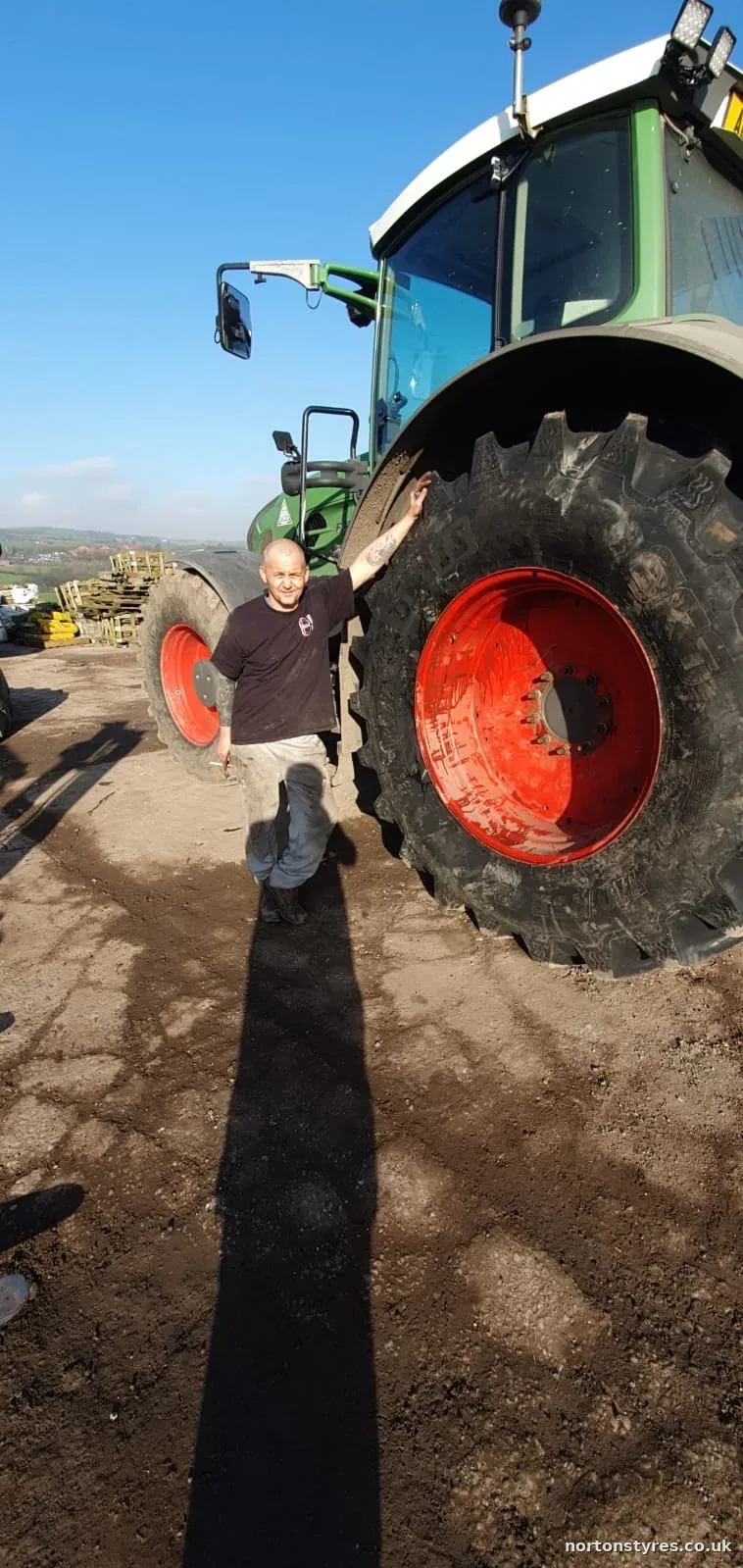 Nortons fitter beside a tractor rear wheel on a farm Nortons fitter beside a tractor rear wheel on a farm