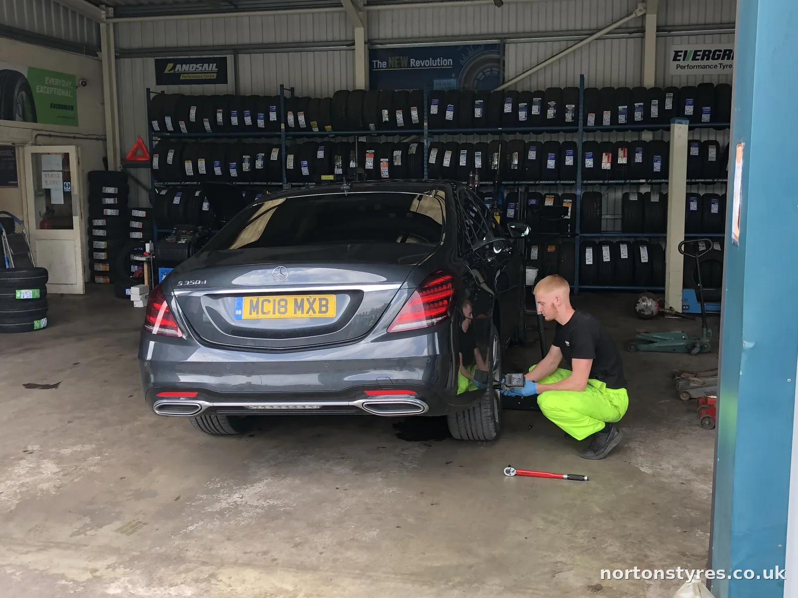 Saloon car in the bay with the fitter at the rear wheel, close view Saloon car in the bay with the fitter at the rear wheel, close view