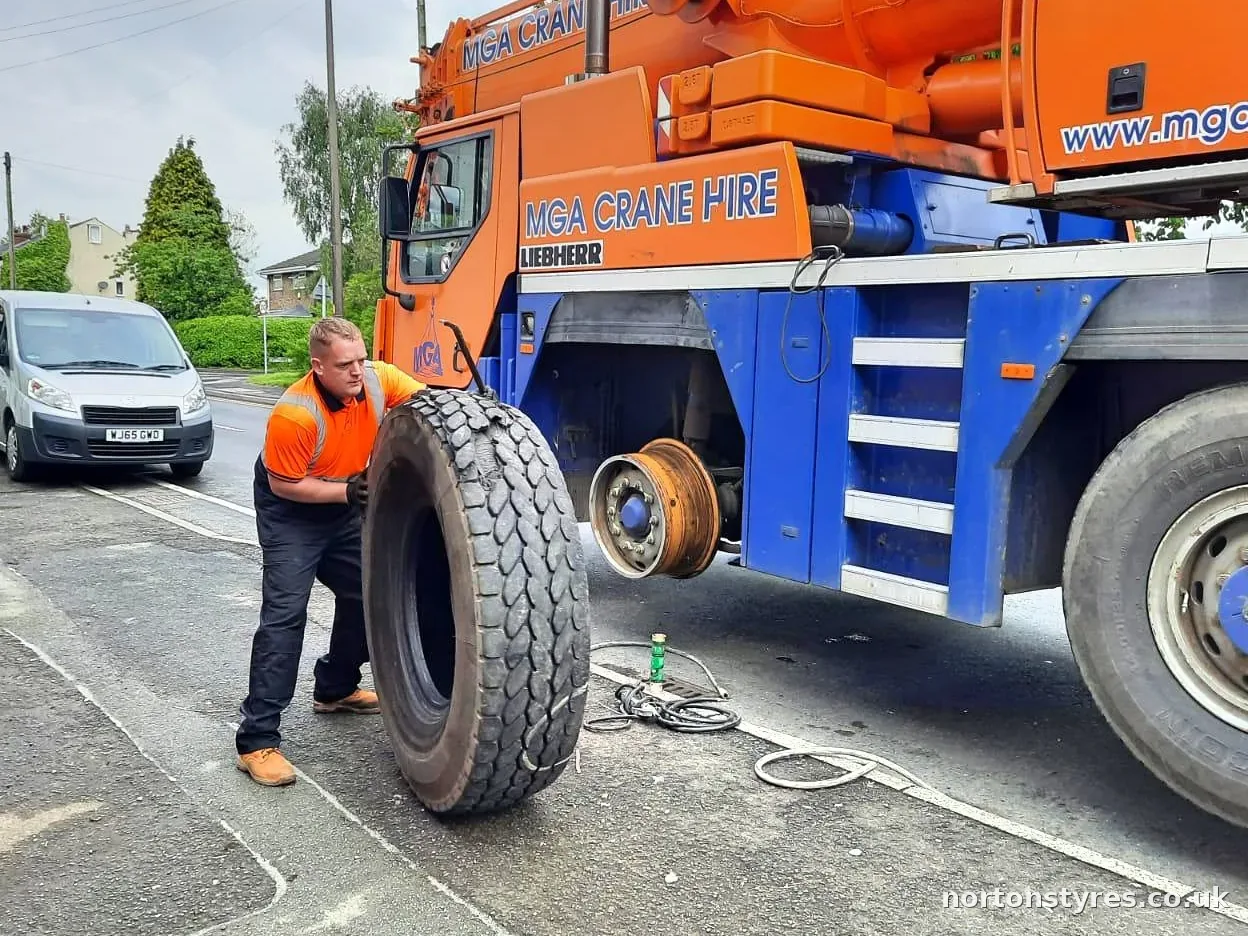 Fitter rolling a new tyre to a mobile crane at the roadside, close view Fitter rolling a new tyre to a mobile crane at the roadside, close view