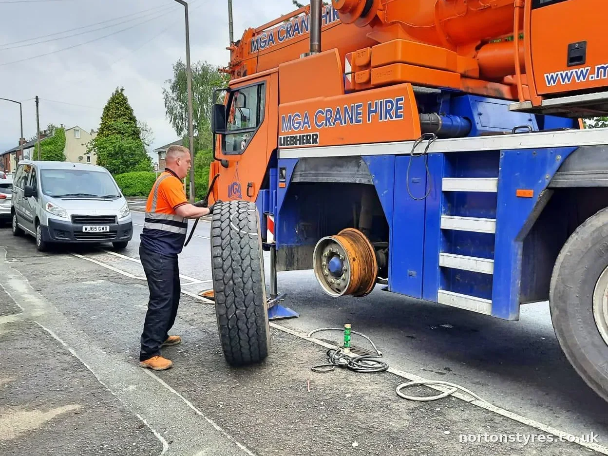 Fitter standing a large crane tyre upright beside the crane, close view Fitter standing a large crane tyre upright beside the crane, close view