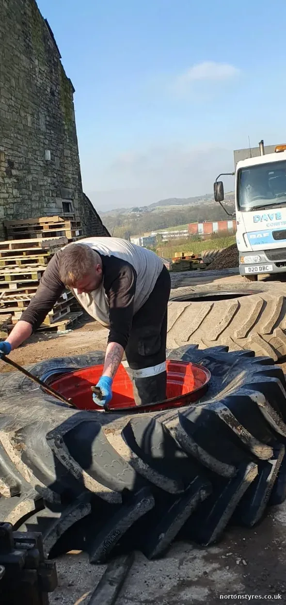 Fitter working on a large tractor tyre on a farm, close view Fitter working on a large tractor tyre on a farm, close view
