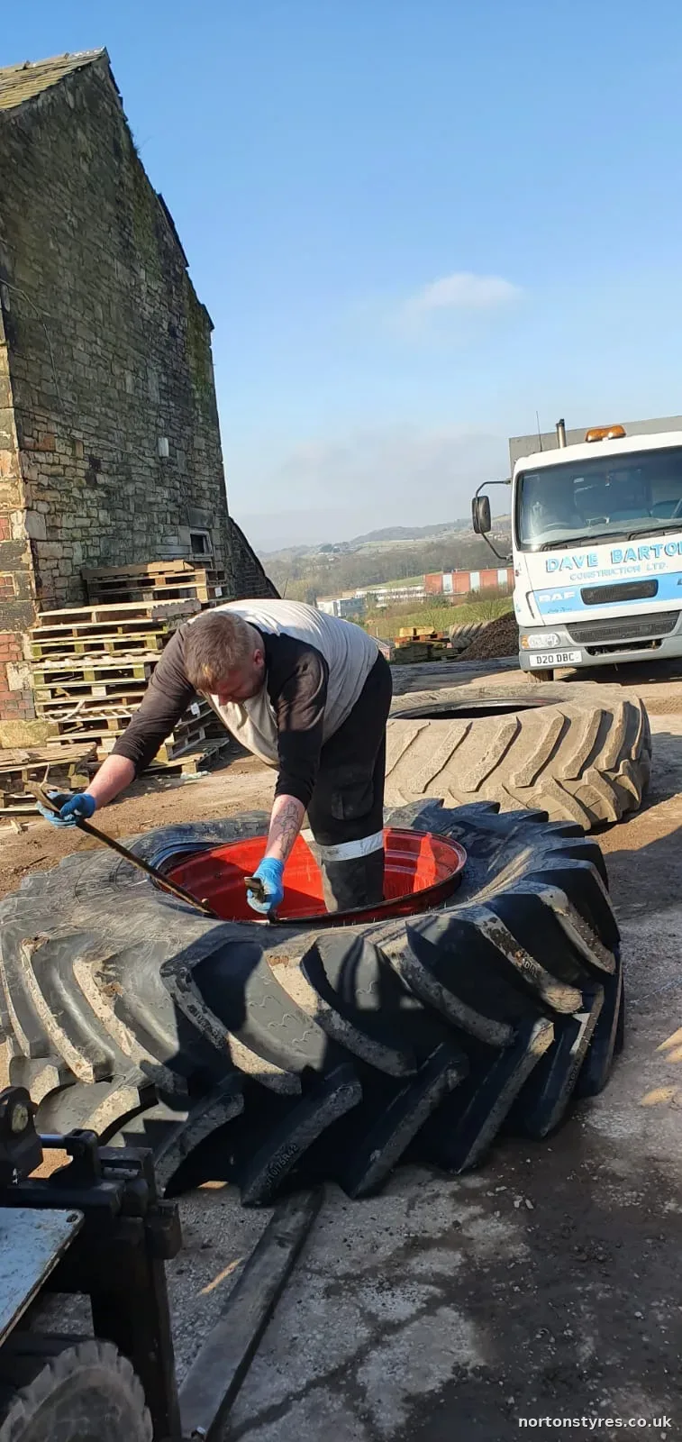 Fitter working on a large tractor tyre on a farm Fitter working on a large tractor tyre on a farm