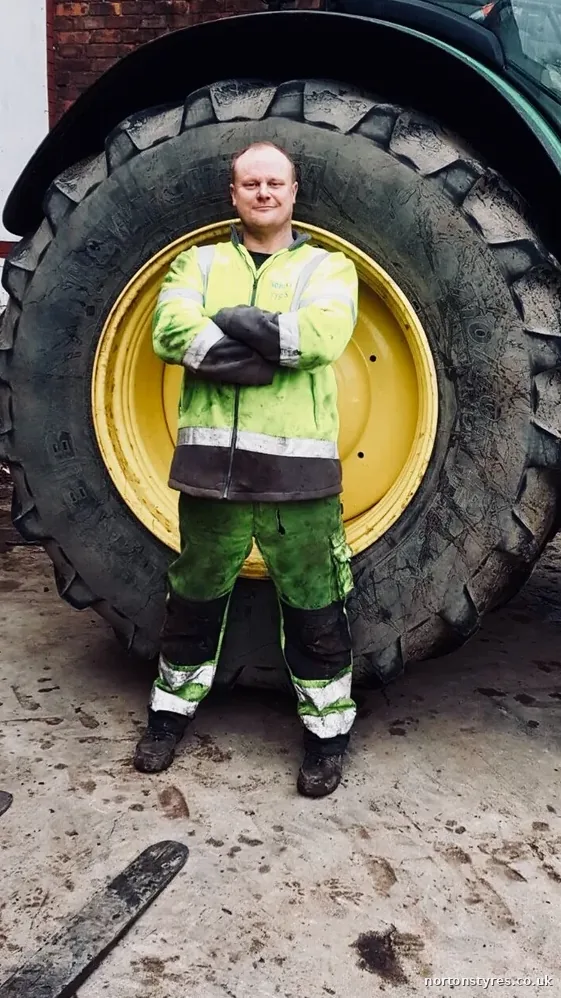 Nortons tyre fitter standing in front of a tractor wheel, close view Nortons tyre fitter standing in front of a tractor wheel, close view