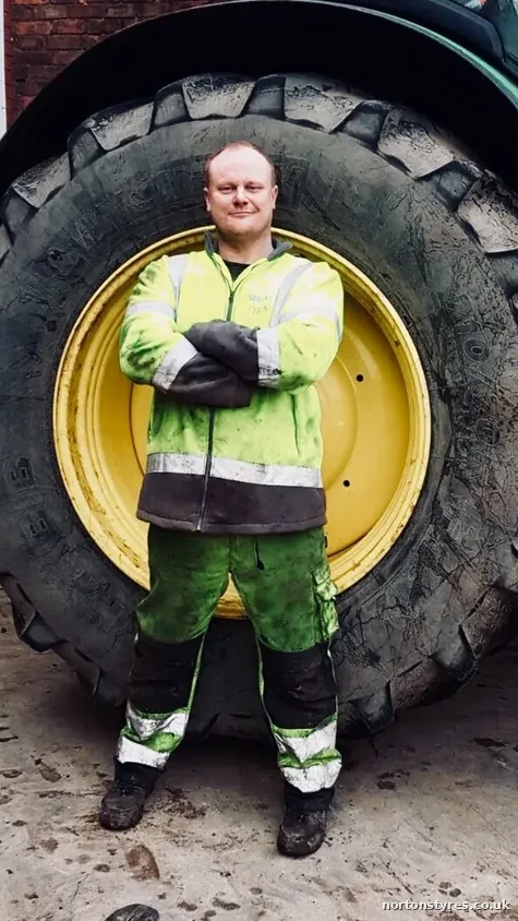 Nortons tyre fitter standing in front of a tractor wheel, detail Nortons tyre fitter standing in front of a tractor wheel, detail