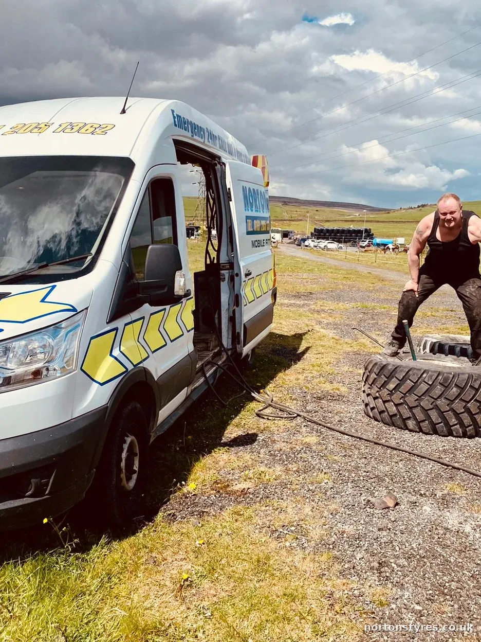 Fitter handling a large tyre beside the Nortons van in a field, close view Fitter handling a large tyre beside the Nortons van in a field, close view