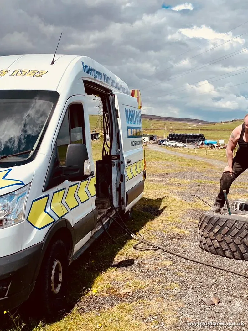 Fitter handling a large tyre beside the Nortons van in a field, detail Fitter handling a large tyre beside the Nortons van in a field, detail