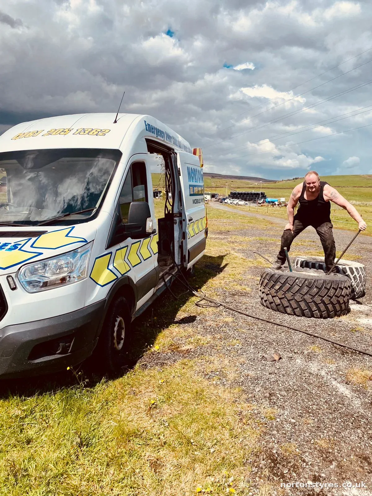 Fitter handling a large tyre beside the Nortons van in a field Fitter handling a large tyre beside the Nortons van in a field