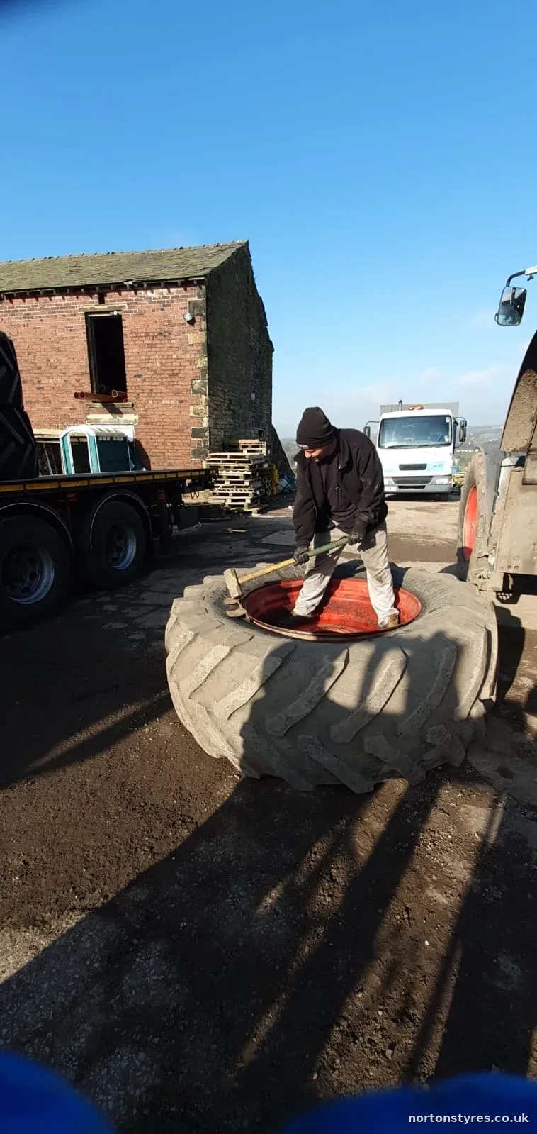 Fitter at a tractor tyre beside a farm building Fitter at a tractor tyre beside a farm building
