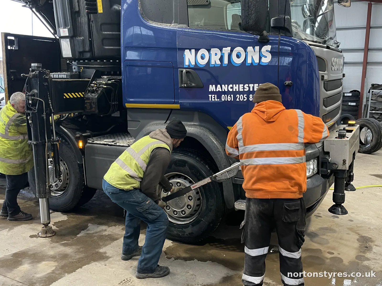 Fitters removing a front wheel from a Nortons lorry, close view Fitters removing a front wheel from a Nortons lorry, close view