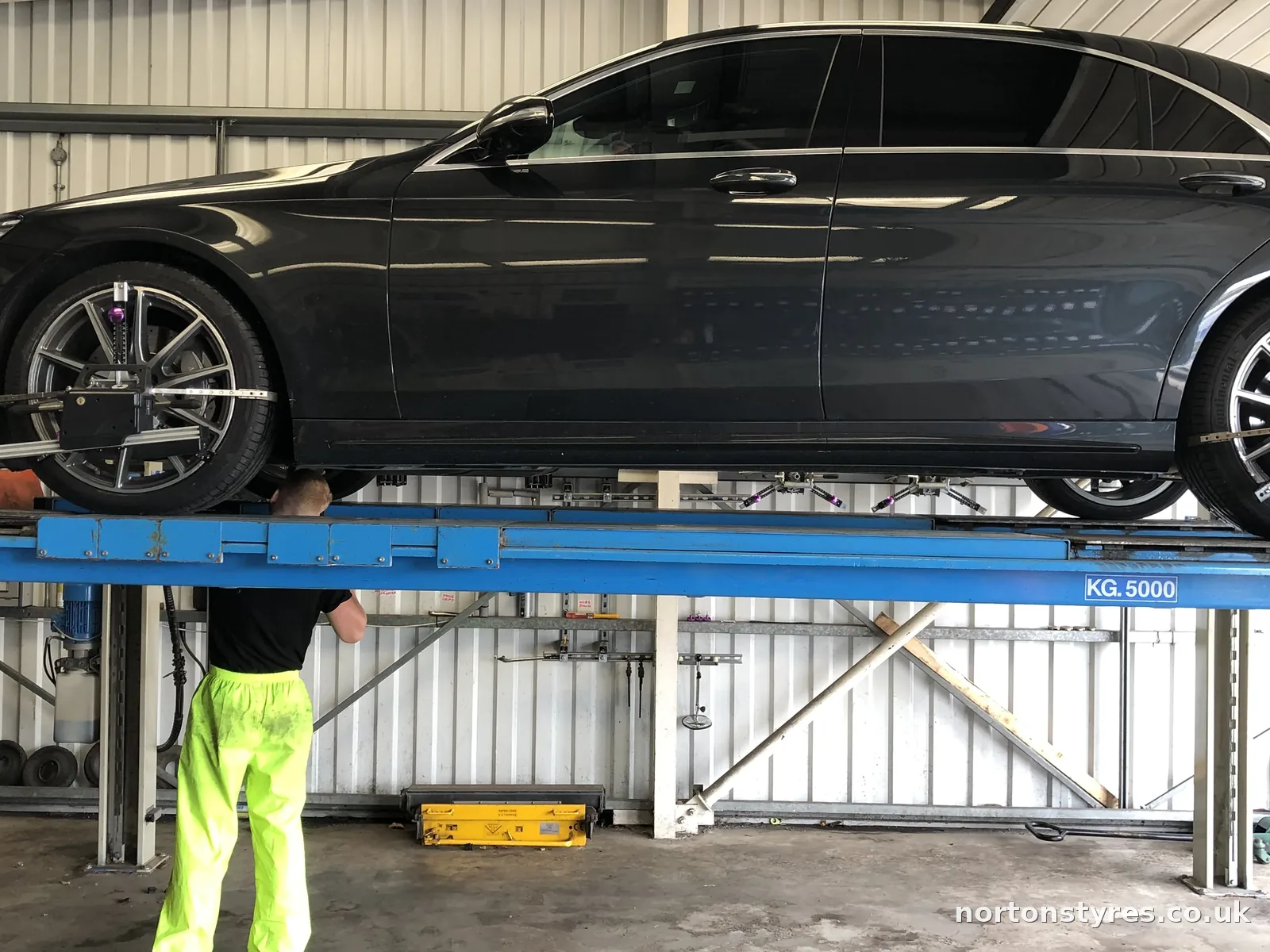 Car on the alignment ramp with the fitter underneath, close view Car on the alignment ramp with the fitter underneath, close view
